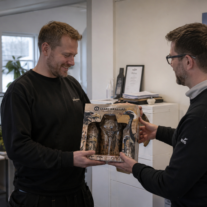 En mand som overrækker en firmajulegave med øl til en medarbejder på et kontor